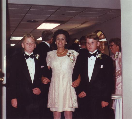 Two boys in tuxedos accompany a woman in a white dress at a festive wedding celebration.