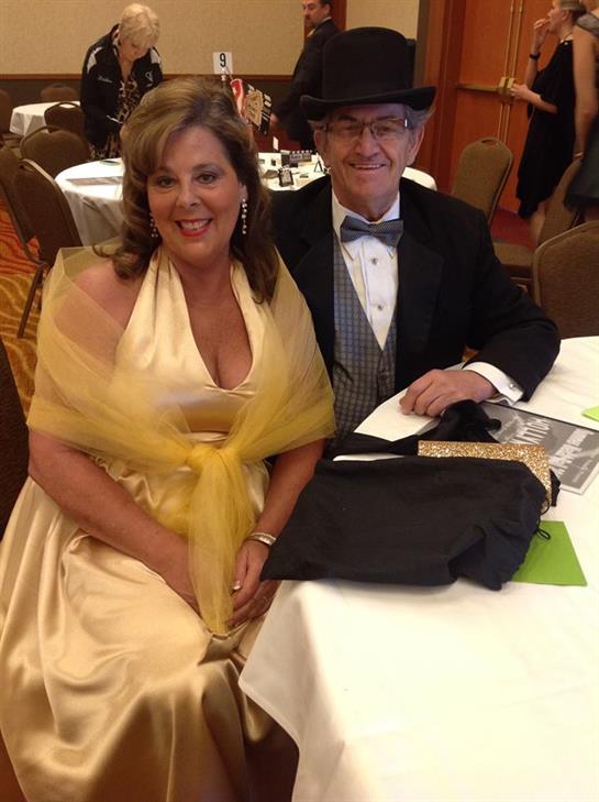 A couple in formal attire poses happily at a banquet table during a special event.