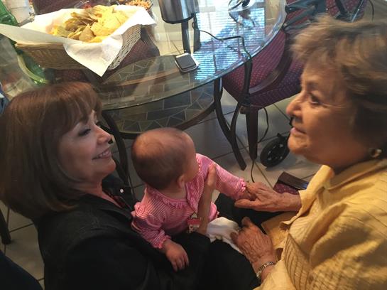 Two women share a joyful moment with a baby during a family gathering in a relaxed setting.