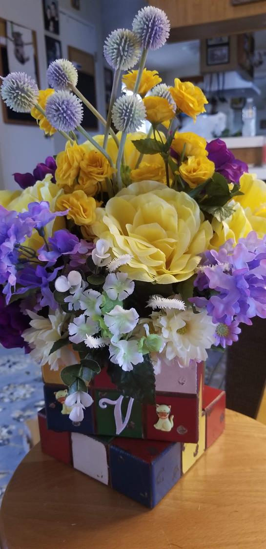 A colorful bouquet of yellow roses, purple blooms, and white accents in a vase.