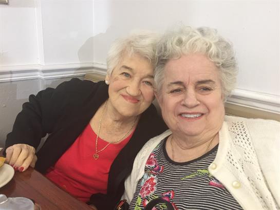 Two smiling elderly women sit together, sharing a joyful moment in a cozy space.