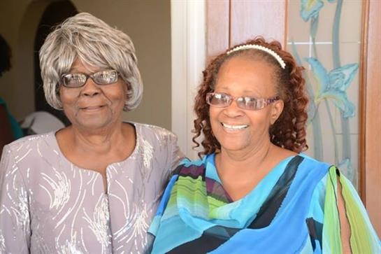 Two smiling women stand together, embracing a moment of joy and connection in a cozy environment.