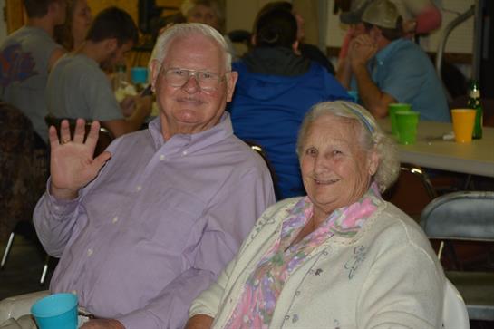 An elderly couple smiles warmly at a lively community gathering.
