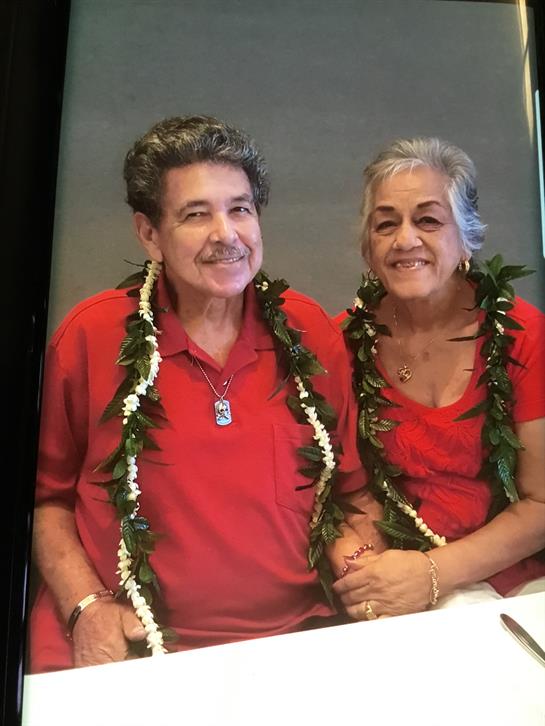 Two happy individuals dressed in matching red attire celebrate together wearing traditional leis.