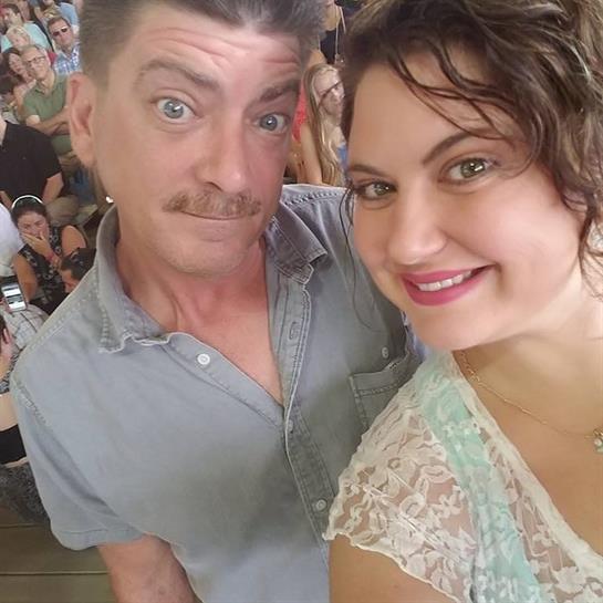 Happy couple takes a selfie surrounded by a lively crowd at a joyful event during daytime.