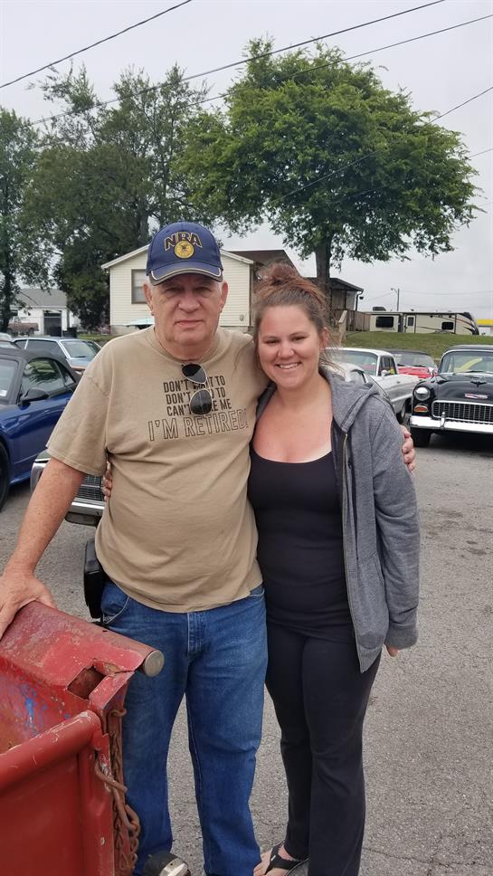 Two people smile together at a car event, enjoying the vintage atmosphere.