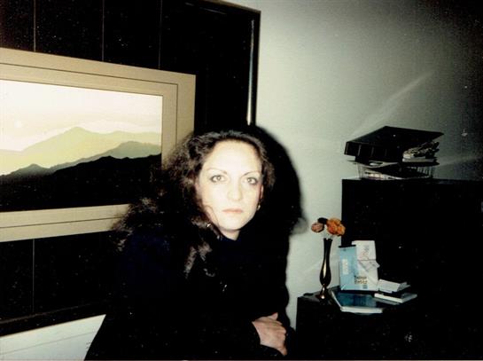Woman with curly hair sits pensively at a desk in a softly lit room with artwork.