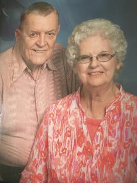An elderly couple smiles warmly while posing for a family portrait at a gathering.