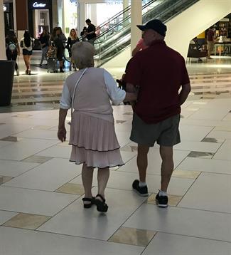 Older couple walks hand in hand through a busy shopping mall during the afternoon.