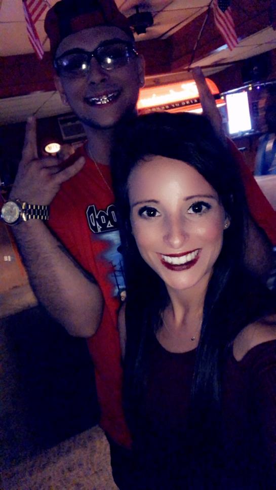 Two friends smile and pose together in a vibrant bar setting during a fun night out.