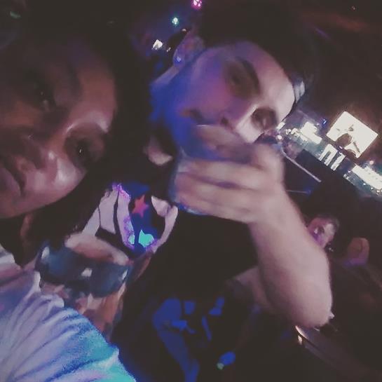 Two friends capture a memorable moment while enjoying a concert with vibrant lights around them.