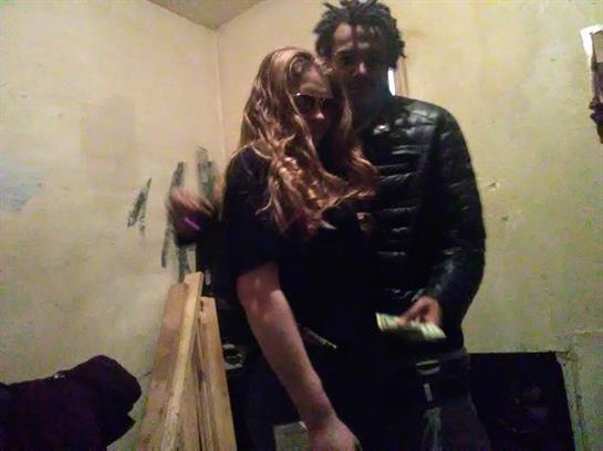 Couple stands closely together in a cozy indoor space, sharing a moment with playful energy.