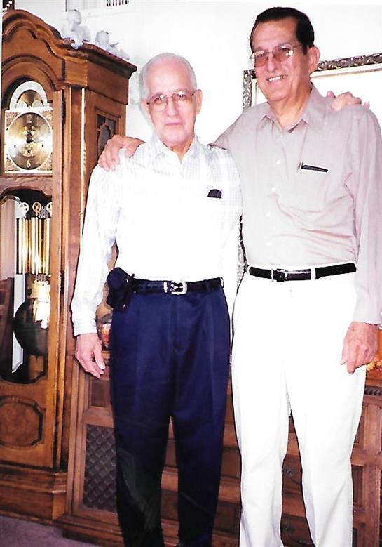 Two elderly men pose together in a warm and inviting living room, smiles on their faces.