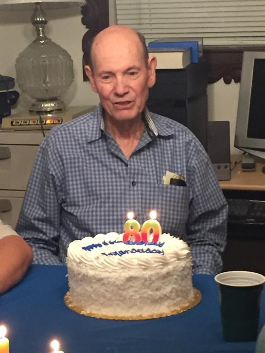 A man is surrounded by loved ones as he celebrates an important birthday with a cake.