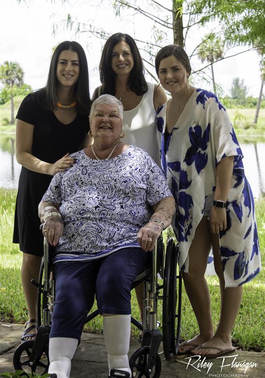 Four women, including a grandmother in a wheelchair, share a joyful moment by a serene lake.