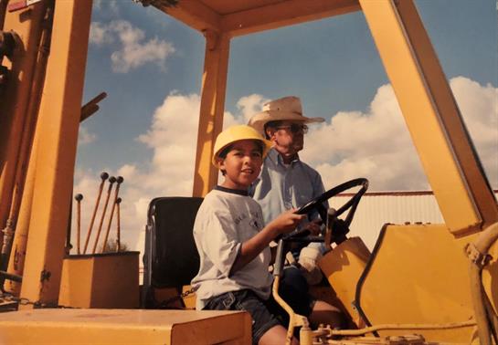 Young boy and girl joyfully steer a construction vehicle while enjoying a sunny day outdoors.