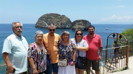 Group of friends gathers on a sunny beach, posing with scenic rock formations in the background.