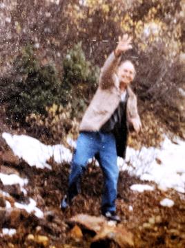 A man is waving enthusiastically while standing on rocky terrain surrounded by sparse snow.