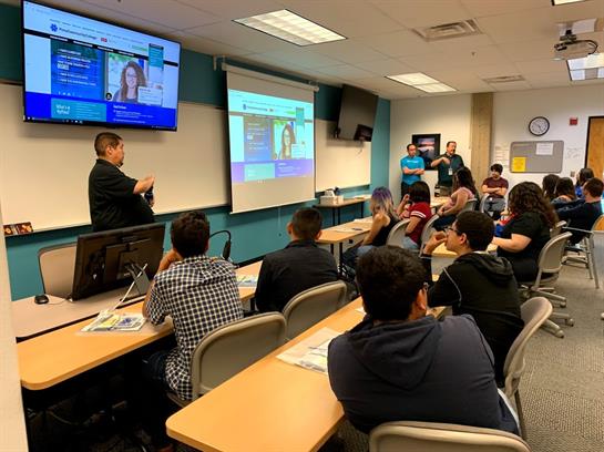 Lecturer explains concepts while students participate actively in a technology-focused lesson.