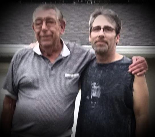 Two men stand side by side, smiling as they enjoy a casual outing in warm weather.
