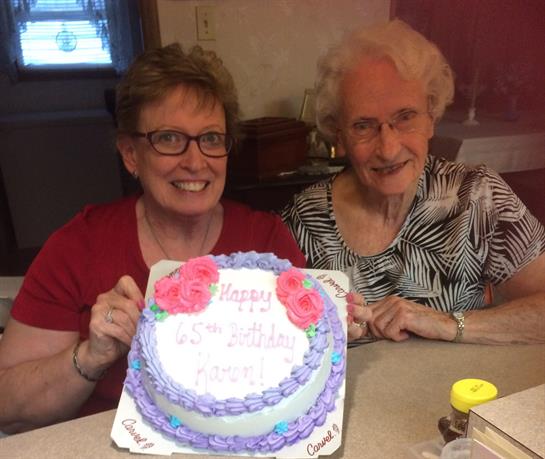 Two women celebrate a birthday together, holding a beautifully decorated cake with roses.