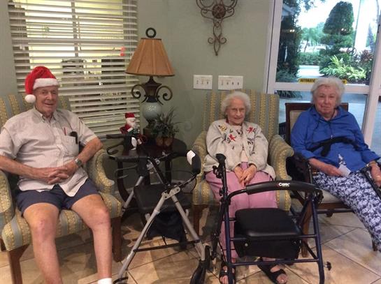 Seniors sit comfortably during a festive event, engaging in conversation and enjoying decorations.