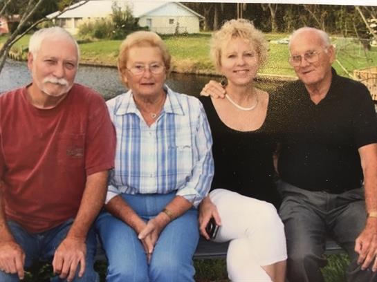 Four individuals sit together by a calm waterway, enjoying their time on a sunny afternoon.