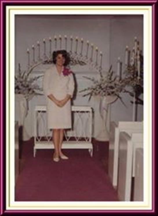 A woman poses in formal attire near elegant decorations featuring candles and flowers in a venue.