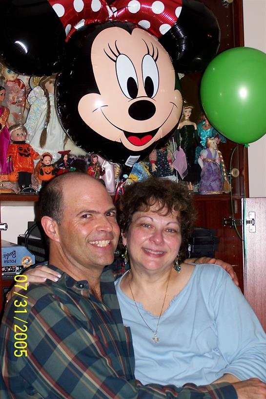 Couple poses joyfully at a party with colorful decorations and a character balloon above them.