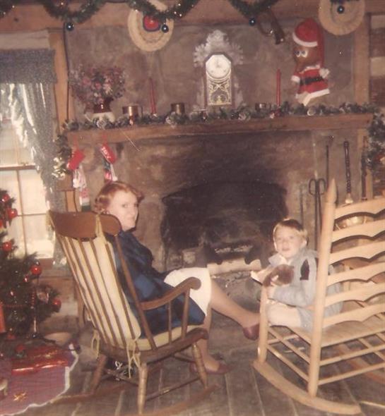 Two children relax in rocking chairs, surrounded by Christmas decorations and cozy warmth.
