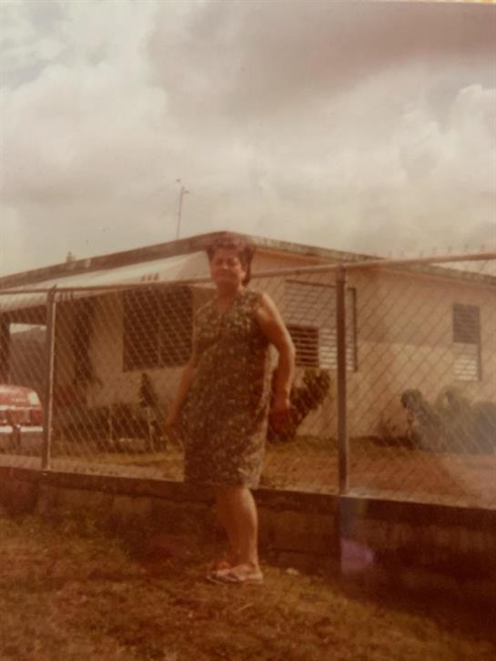A woman stands confidently by a fence, showcasing her casual dress in a quaint rural setting.