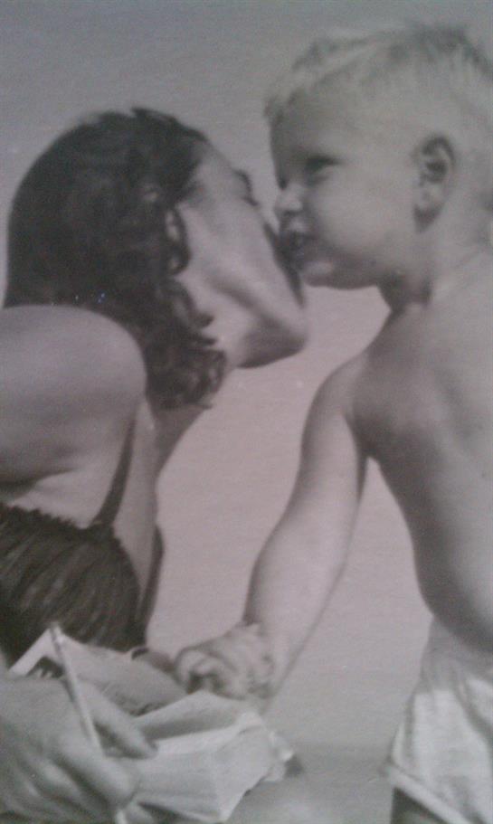 A mother shares a tender kiss with her infant in a cozy indoor setting, capturing joy and love.