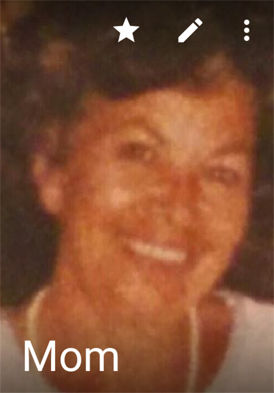 A joyful woman is smiling warmly, surrounded by a friendly atmosphere during a sunny outdoor event.