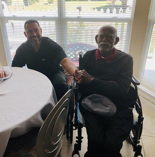 Two men enjoy a heartfelt moment at a table in a senior center during a family gathering.