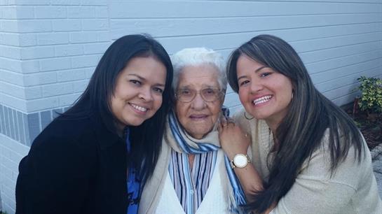 Two women smile broadly while posing with an elderly woman in a warm, inviting environment.