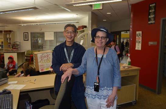 Two people are joyfully standing side by side at a community center, celebrating summer.