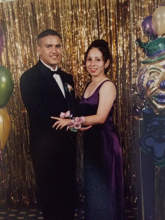 Couple poses together in formal attire amidst vibrant decorations at a celebratory event.