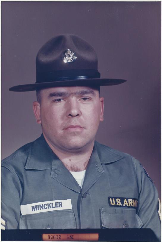 A military drill instructor stands confidently in uniform, sporting a distinctive hat while posing.