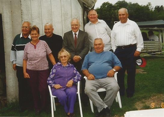 Group of people enjoying a joyful reunion outdoors at a rural setting on a sunny day.
