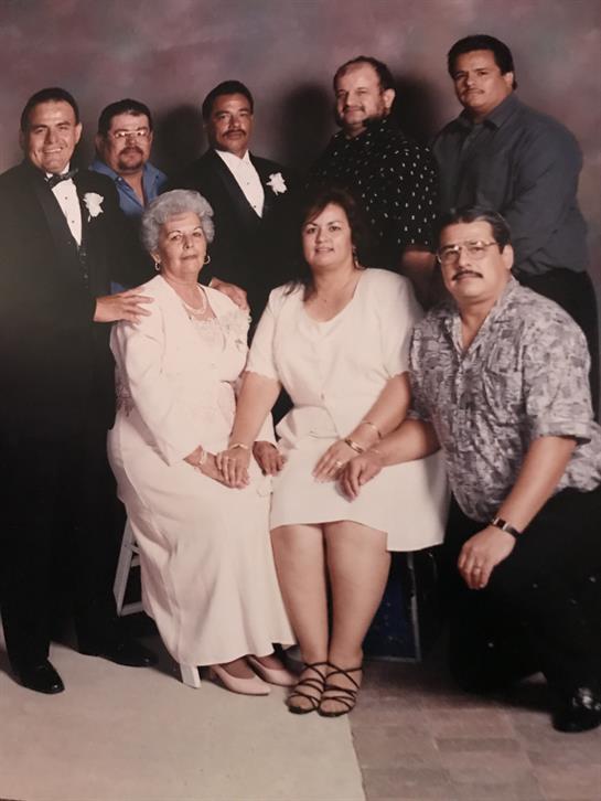 A formal family gathering features seven adults and two women dressed elegantly, sharing smiles.