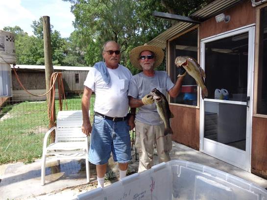 Two men stand together holding large fish, celebrating their successful day fishing.