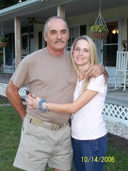 A man and a woman smile while standing close together in a backyard at dusk.