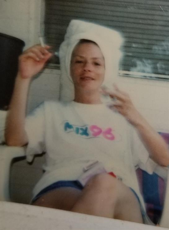 A woman is sitting comfortably at home, wearing a t-shirt and towel, enjoying her leisure time.