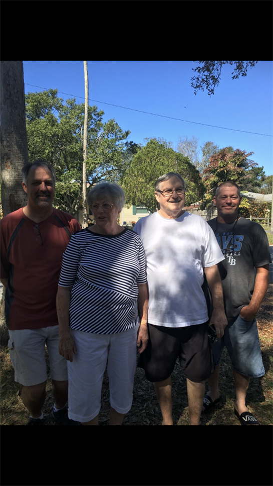 Four family members stand together outside, enjoying a sunny day in a residential area.