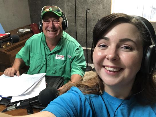 Two radio hosts smile as they engage listeners while broadcasting from the studio together.