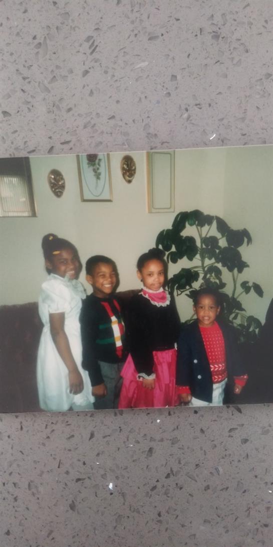 Four children stand smiling in traditional attire, celebrating a joyful holiday occasion indoors.