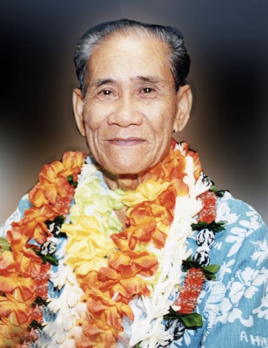 Elderly man in a floral shirt and colorful leis smiles at a festive gathering.
