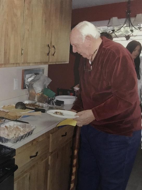 Elderly man carefully serves a plate of food at a warm family gathering in a kitchen.