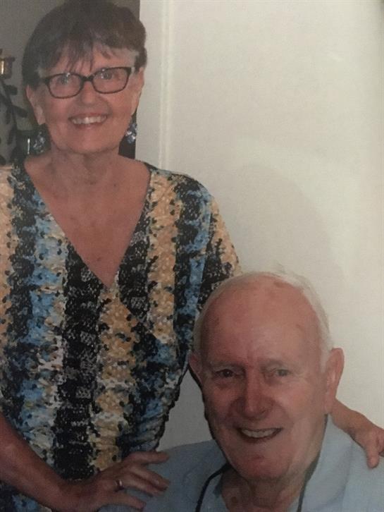 A couple poses for a picture, both smiling happily while enjoying each other's company indoors.
