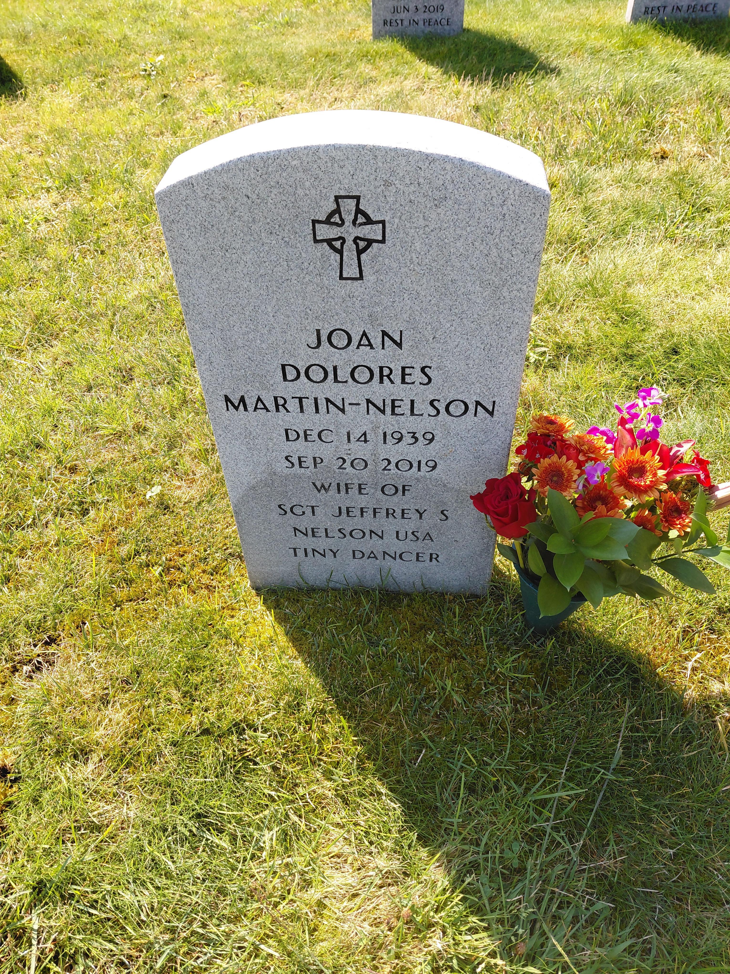 Gravestone marks the resting place of Joan Dolores Martin-Nelson, adorned with colorful flowers.